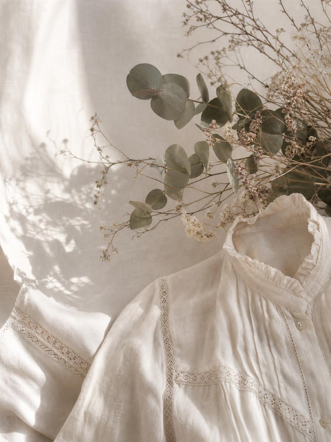 A vintage linen blouse with lace trim beside dried eucalyptus and baby's breath.